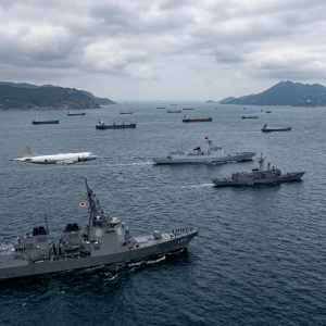 Japanese naval ships sailing with patrol aircraft flying nearby near cargo ships and mountains